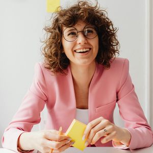 Professional leadership coach planning client goals with colorful sticky notes, wearing a pink blazer and glasses, demonstrating the organized and positive approach to private coaching and personal development