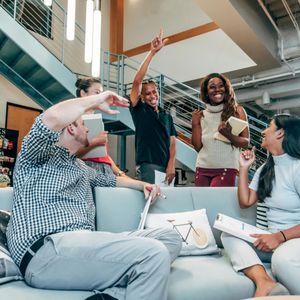 Group leadership coaching session showing diverse professionals celebrating success in a casual office lounge, demonstrating the energetic and collaborative nature of team development and workplace coaching